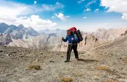 Trekker avec sac à dos rouge marchant sur un sentier de haute montagne au Tadjikistan