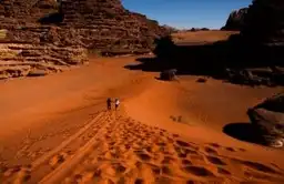 Deux voyageurs marchant sur une crête de dune de sable rouge dans le désert du Wadi Rum en Jordanie