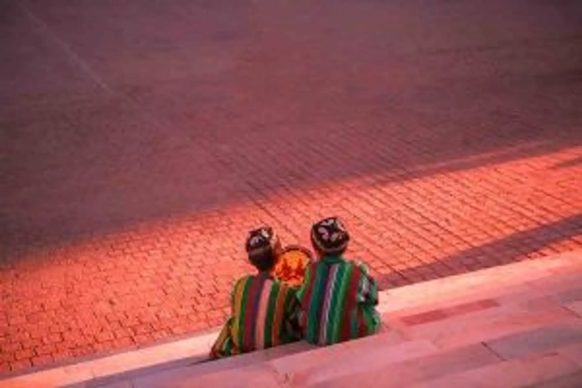 Voyage en Ouzbékistan — Deux hommes en costume traditionnel discutant sur les marches d'un monument au coucher du soleil.