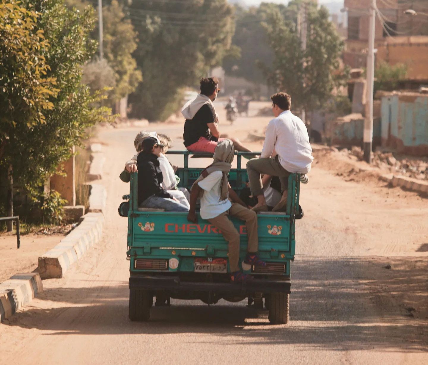 Voyage en Égypte – habitants assis à l’arrière d’un pick-up sur une route bordée de végétation