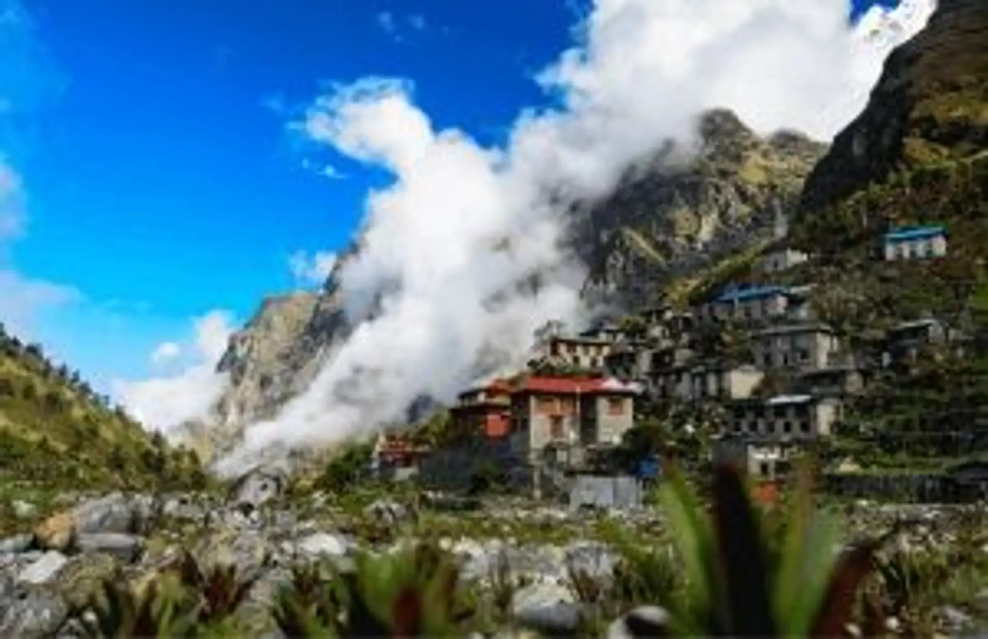 Voyage au Népal — Village traditionnel en pierre accroché au flanc des montagnes de l'Himalaya sous un ciel bleu.