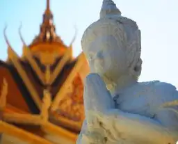 Statue de divinité bouddhique devant la toiture sculptée d'un temple à Phnom Penh Cambodge