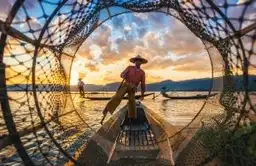 Pêcheur traditionnel ramant avec sa jambe sur une barque au milieu d'un filet conique sur le lac Inle en Birmanie.