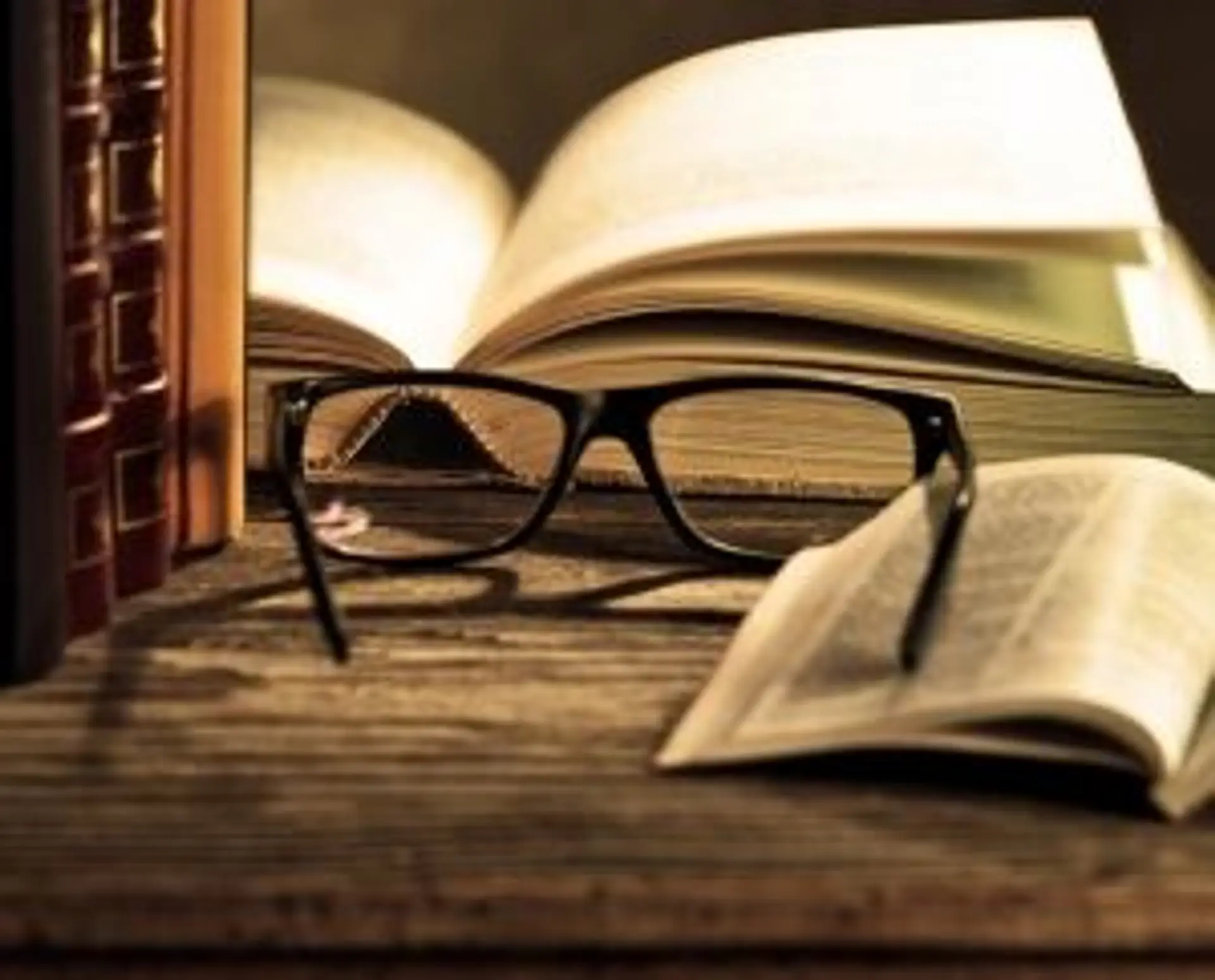 Travel in Asia - A pair of reading glasses on a wooden table surrounded by open and closed books