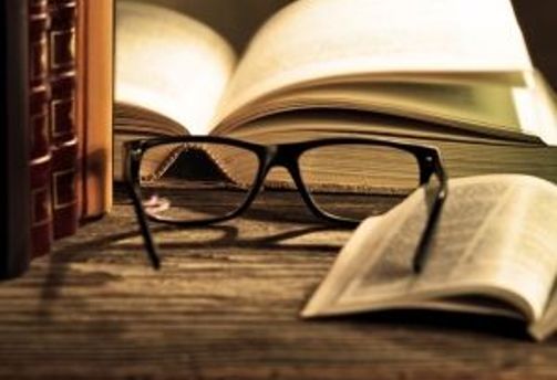 Travel in Asia - A pair of reading glasses on a wooden table surrounded by open and closed books
