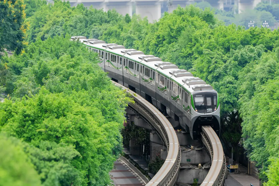 Voyager en train en Chine – Monorail de Chongqing serpentant sur sa voie aérienne au milieu d'une végétation dense.
