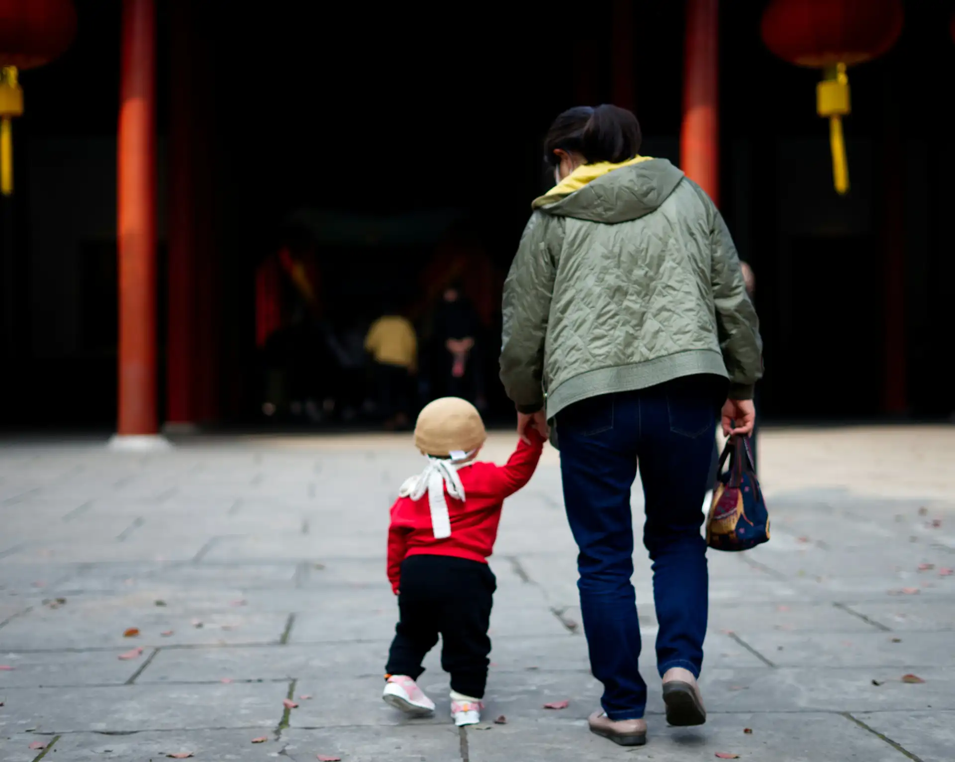 Un adulte et un jeune enfant marchant main dans la main devant l'entrée d'un temple traditionnel en Chine.