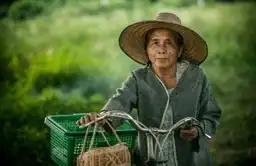 Femme thaïlandaise à vélo transportant un panier, illustrant la mobilité douce et le tourisme durable en Thaïlande.