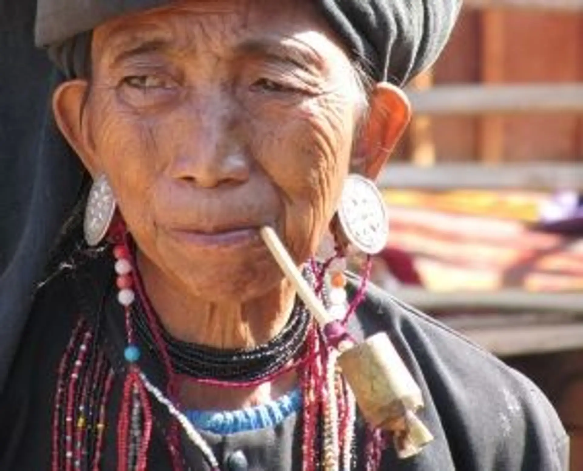 Travel in Asia - An older woman of the Small Ann Tribe in traditional attire smoking a pipe.