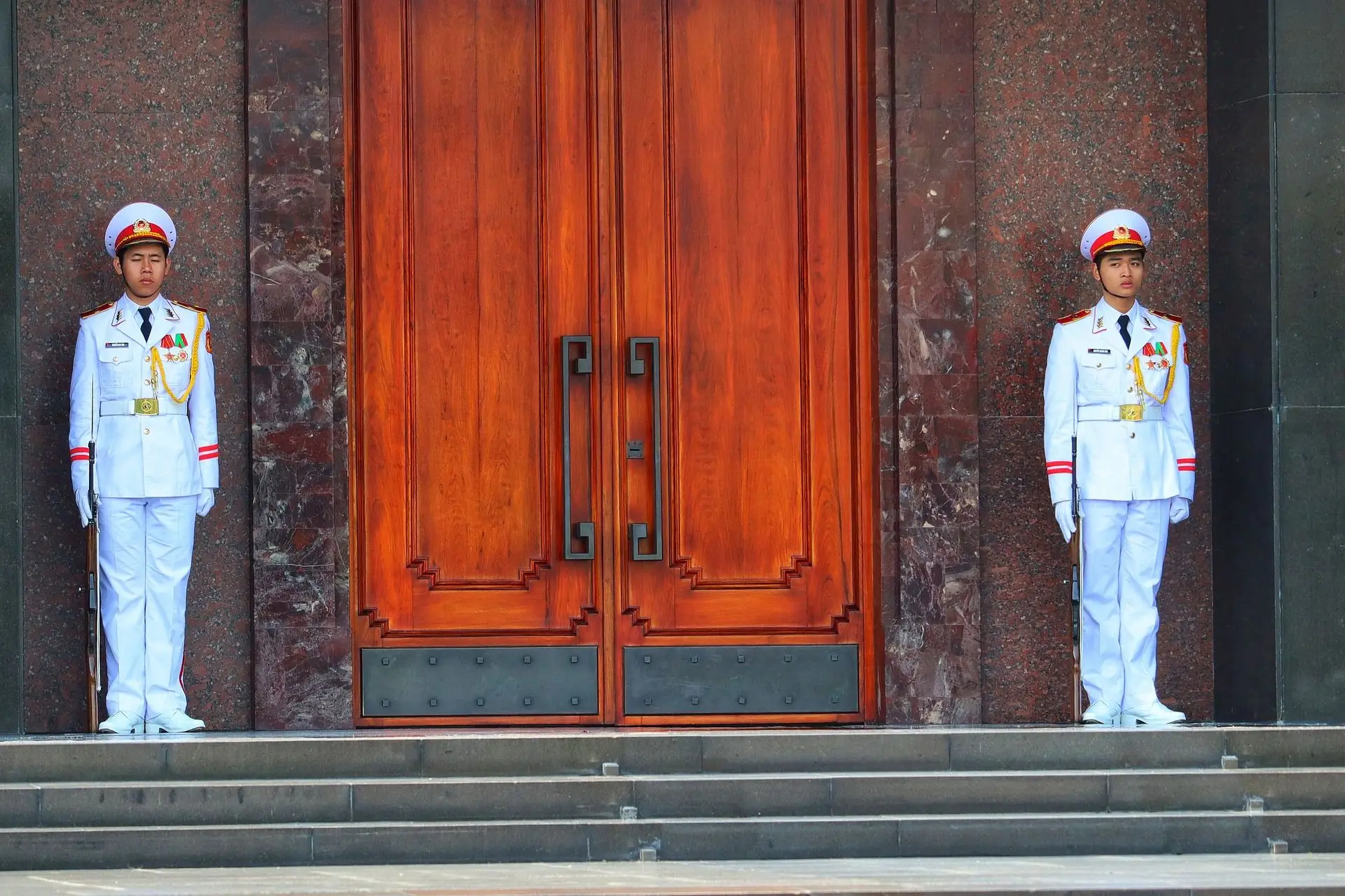 Travel in Asia - Two soldiers in white uniforms guard a wooden door outside the Ho Chi Minh Mausoleum in Hanoi, Vietnam