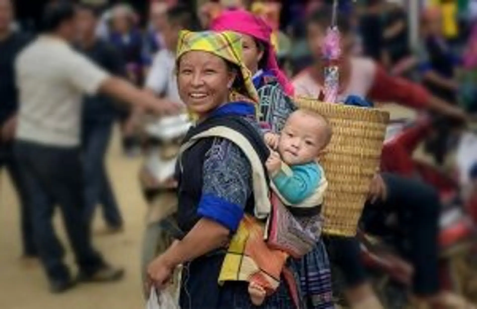 Travel in Asia - A person carrying a baby on their back walking through a busy marketplace in Vietnam