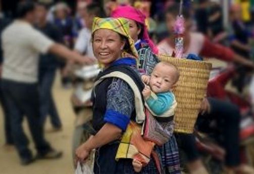 Travel in Asia - A person carrying a baby on their back walking through a busy marketplace in Vietnam