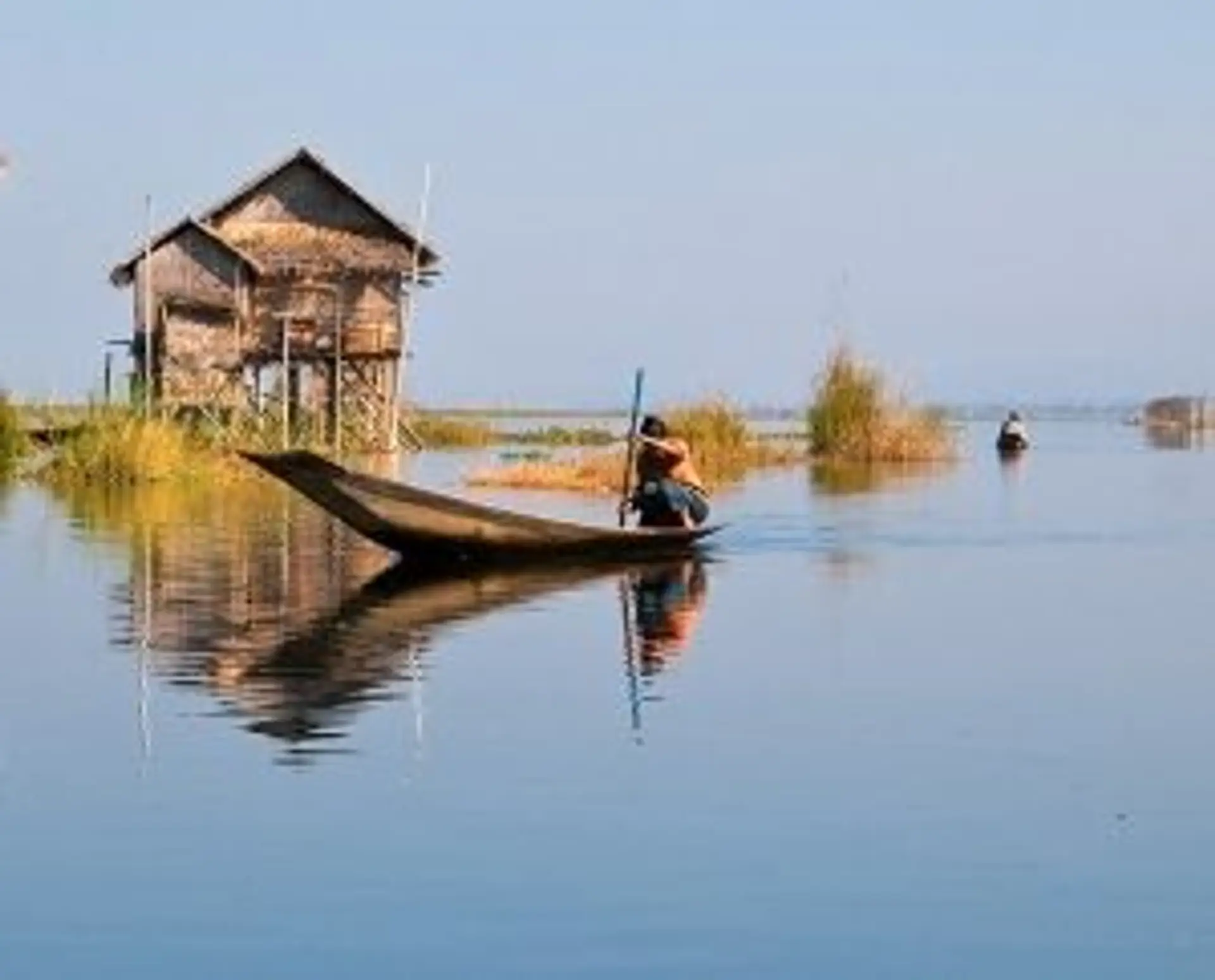 Travel in Asia - Man navigating a boat in front of a stilt house on Inle Lake in Myanmar.