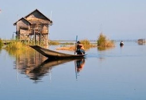 Travel in Asia - Man navigating a boat in front of a stilt house on Inle Lake in Myanmar.