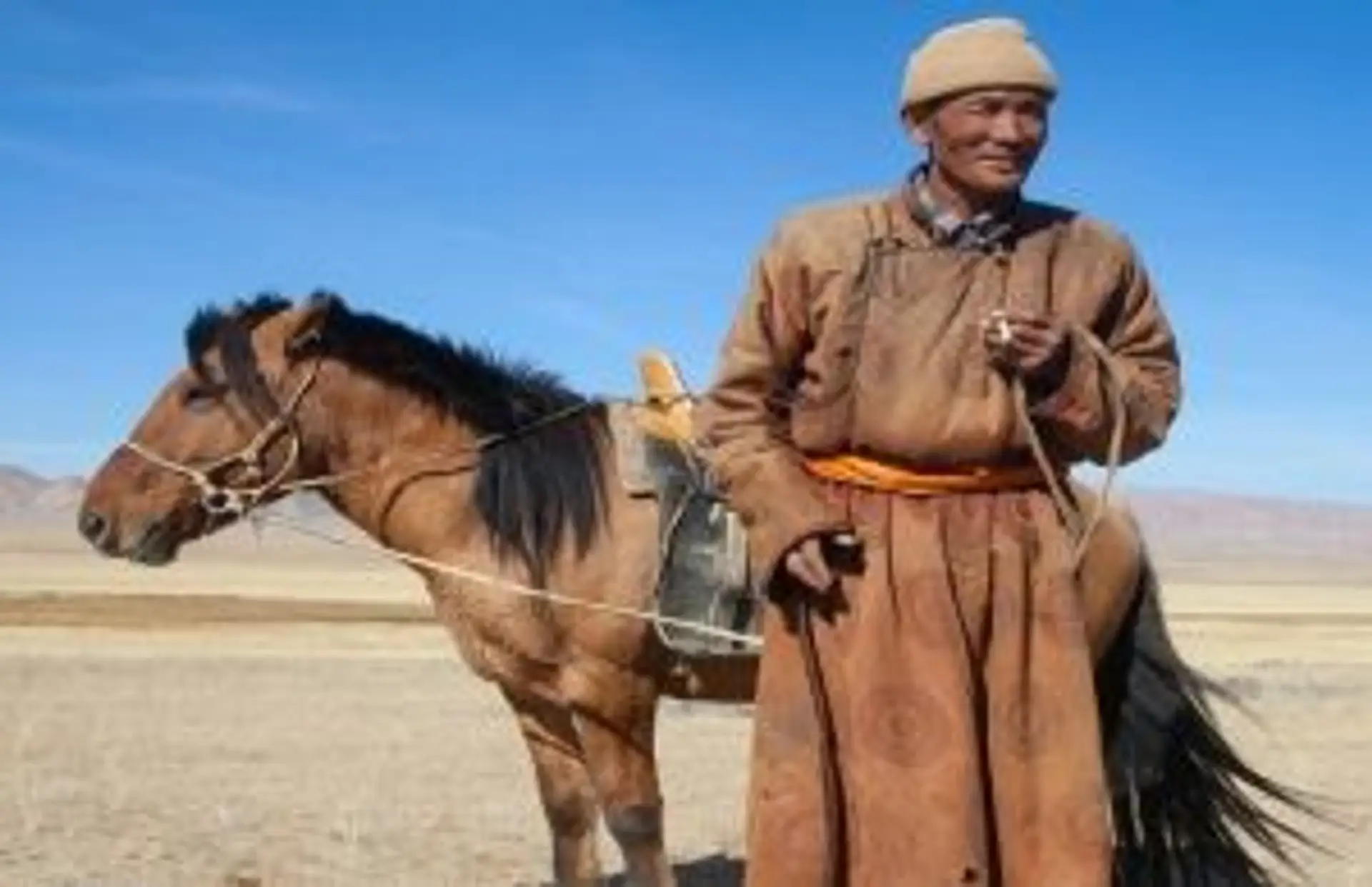 Voyage en Mongolie — Un cavalier nomade en tenue traditionnelle avec son cheval dans l'immensité de la steppe mongole.