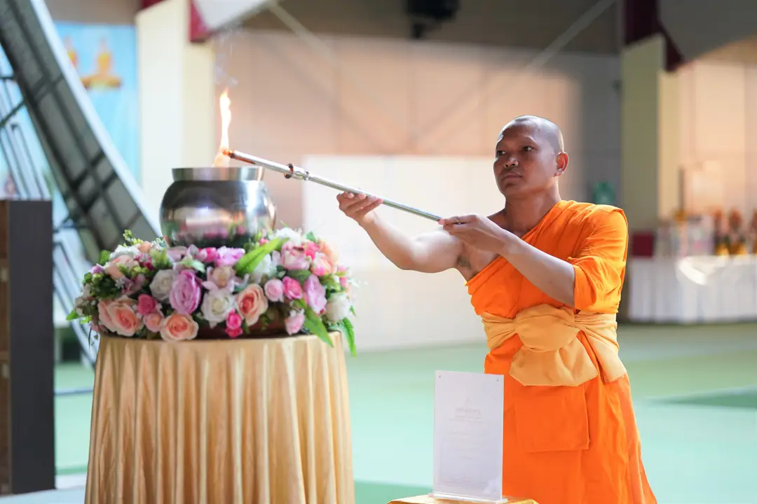 Moine bouddhiste en robe orange allumant une flamme sacrée sur un vasque fleurie lors d'une cérémonie rituelle au Laos.