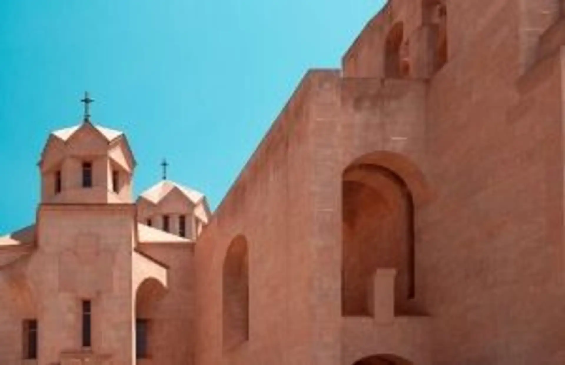 Façade en pierre ocre d'une église apostolique arménienne sous un ciel bleu pur, témoignant du patrimoine chrétien du pays.