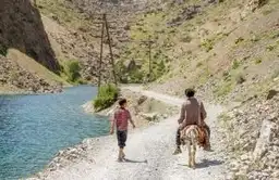 Voyageurs sur une piste de montagne longeant une rivière turquoise dans les paysages sauvages du Tadjikistan.