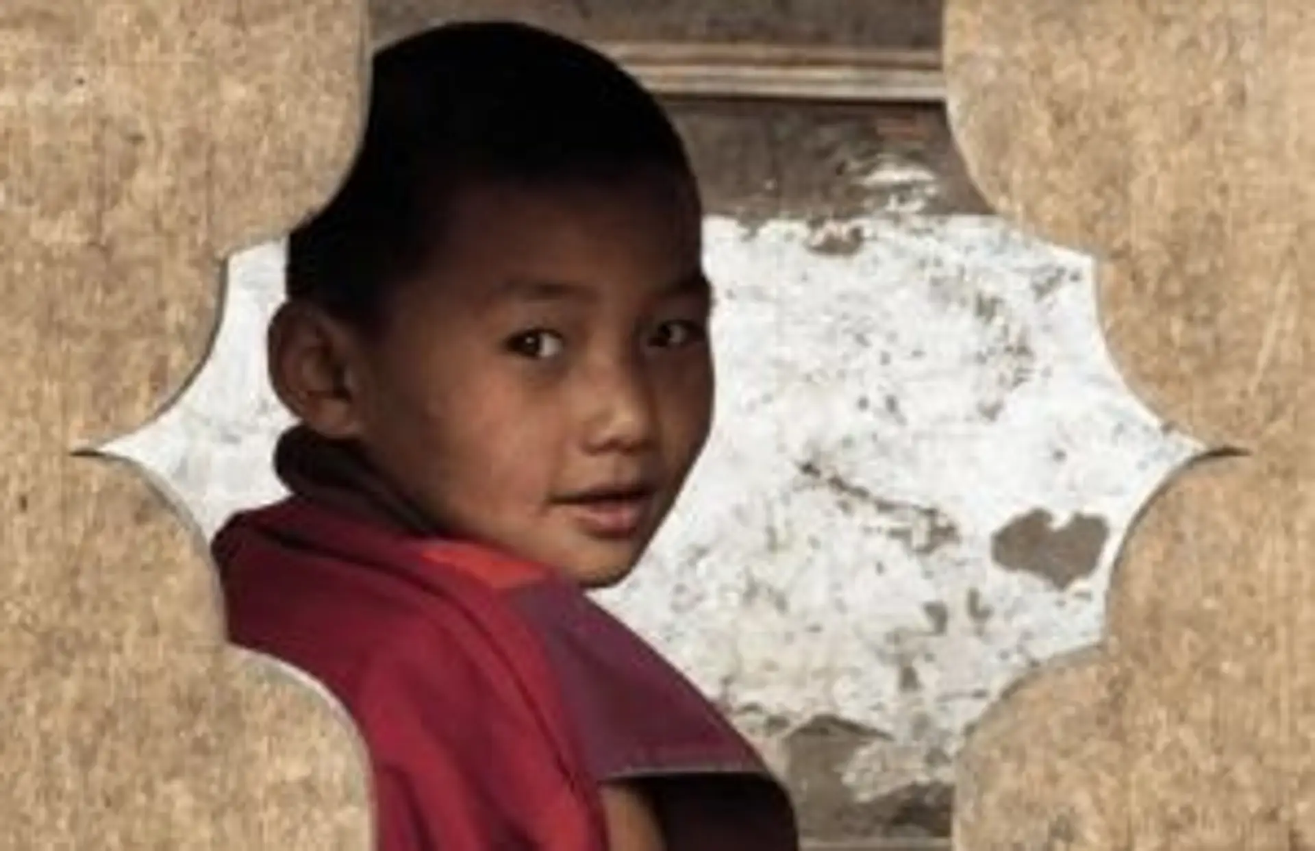 Portrait d'un jeune moine bouddhiste en robe traditionnelle rouge regardant vers l'objectif au Bhoutan.