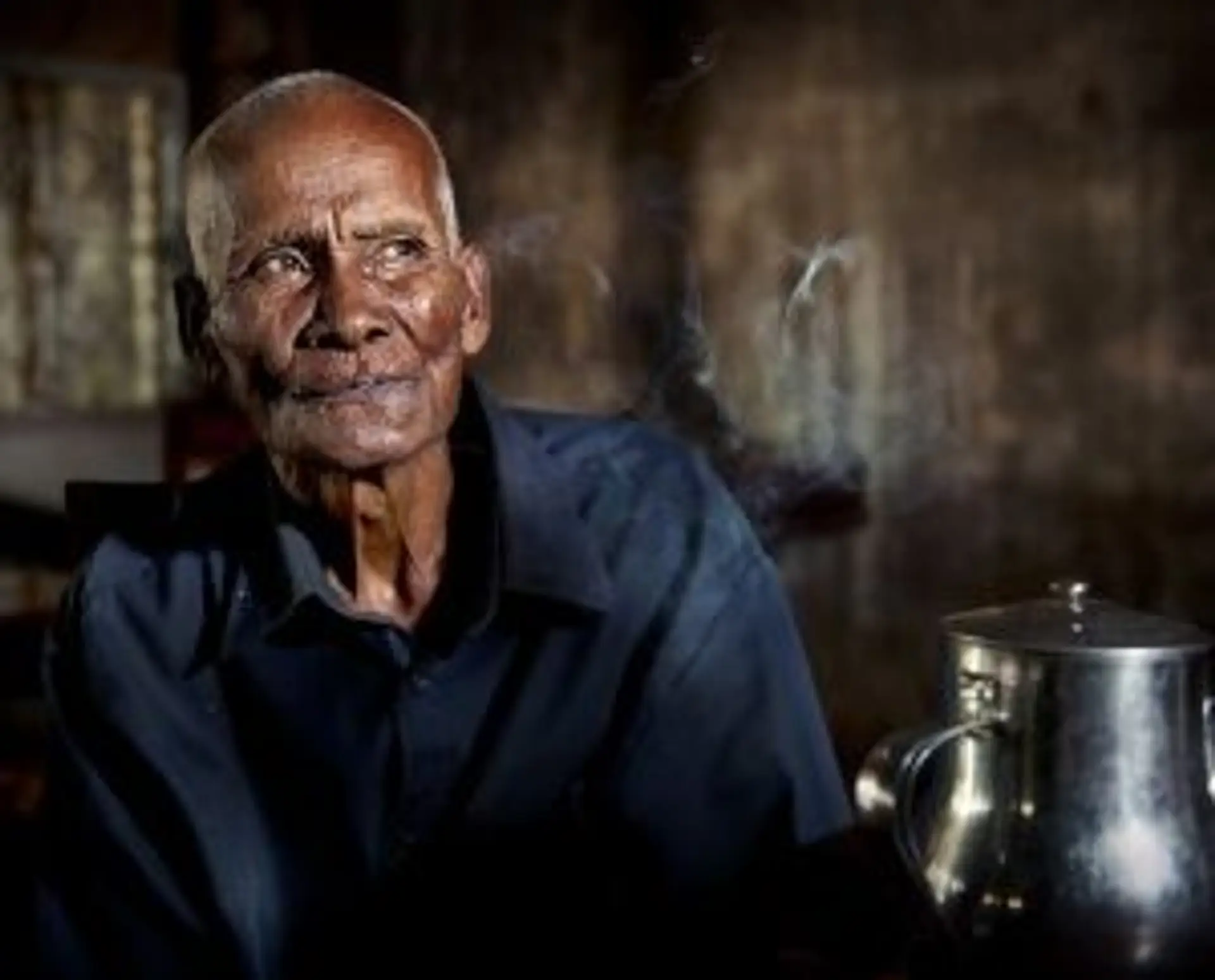 Portrait d'un homme âgé cambodgien au regard serein dans un intérieur traditionnel à la lumière naturelle.