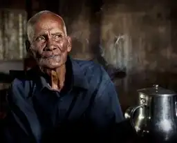 Portrait d'un homme âgé cambodgien au regard serein dans un intérieur traditionnel à la lumière naturelle.