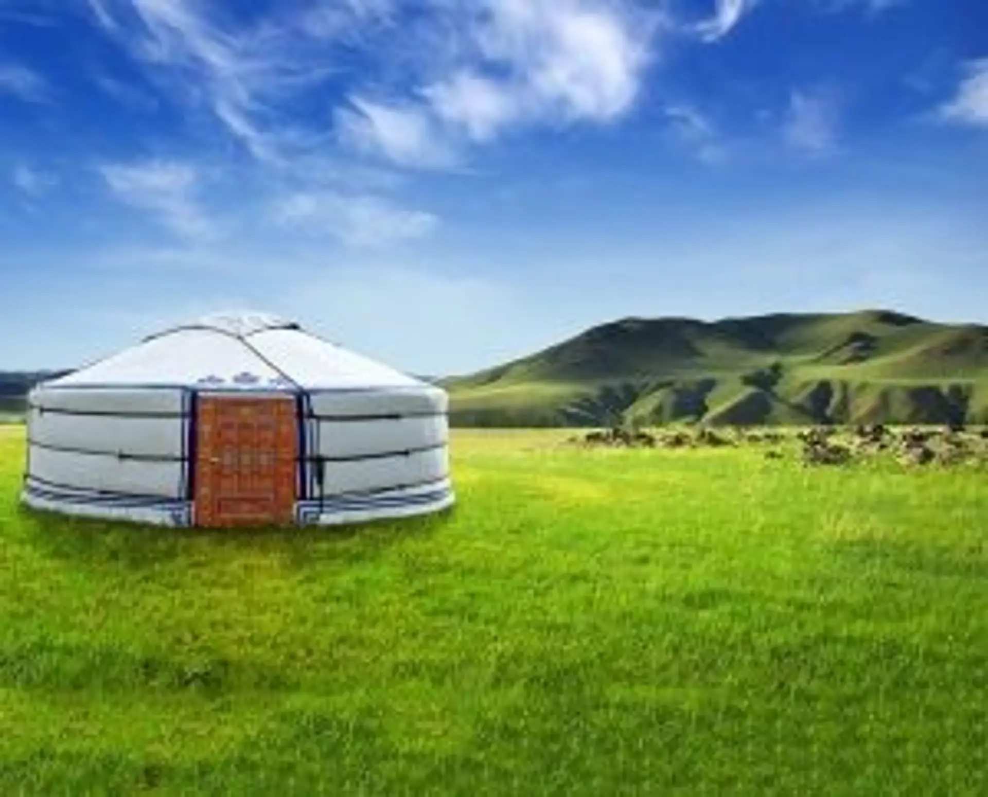 Voyage en Mongolie — Une yourte traditionnelle installée au cœur d'une vaste steppe verdoyante sous un ciel bleu.