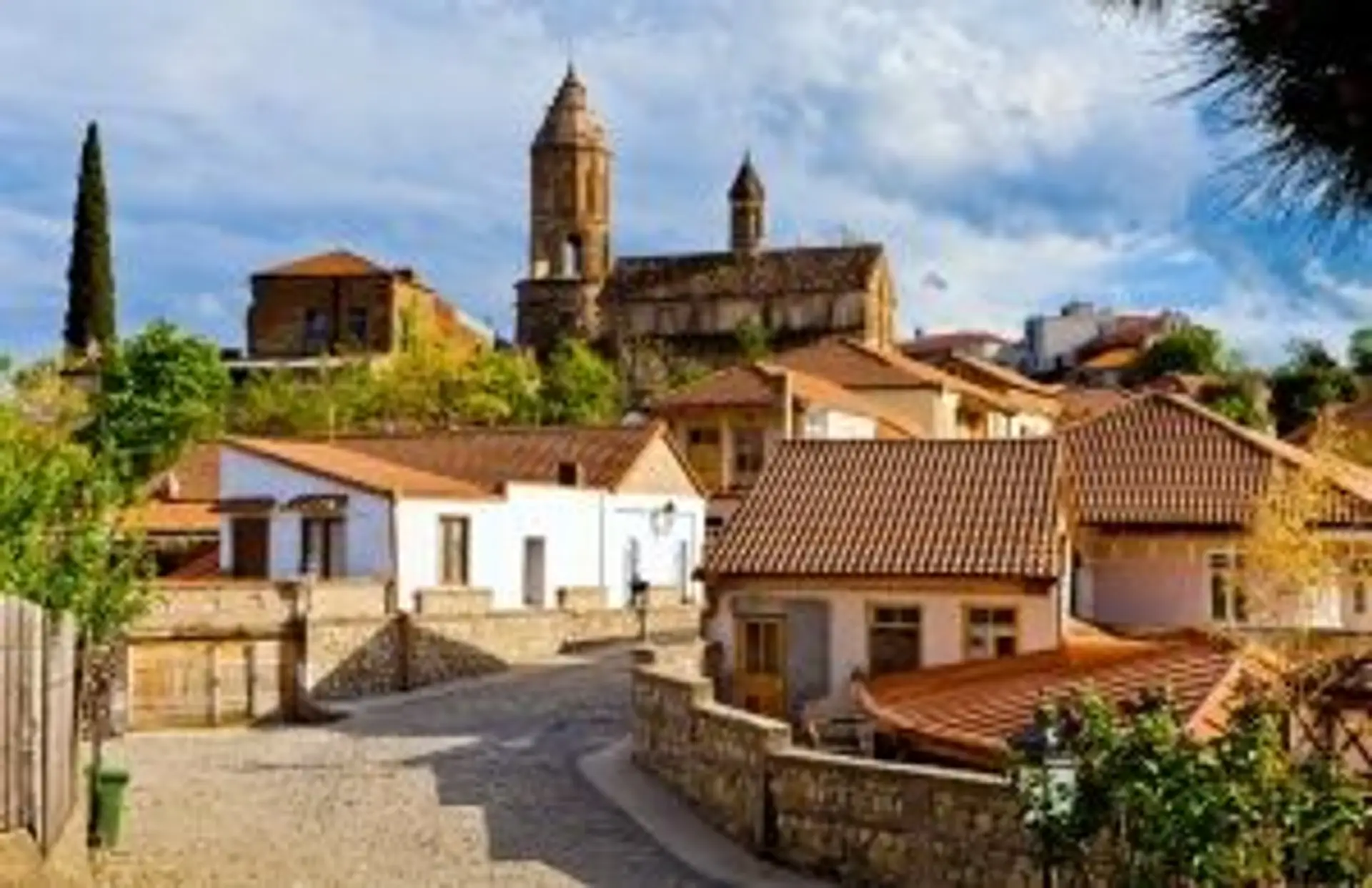 Voyage en Géorgie — Village de montagne aux toits de tuiles et église orthodoxe sous un ciel bleu d'été.