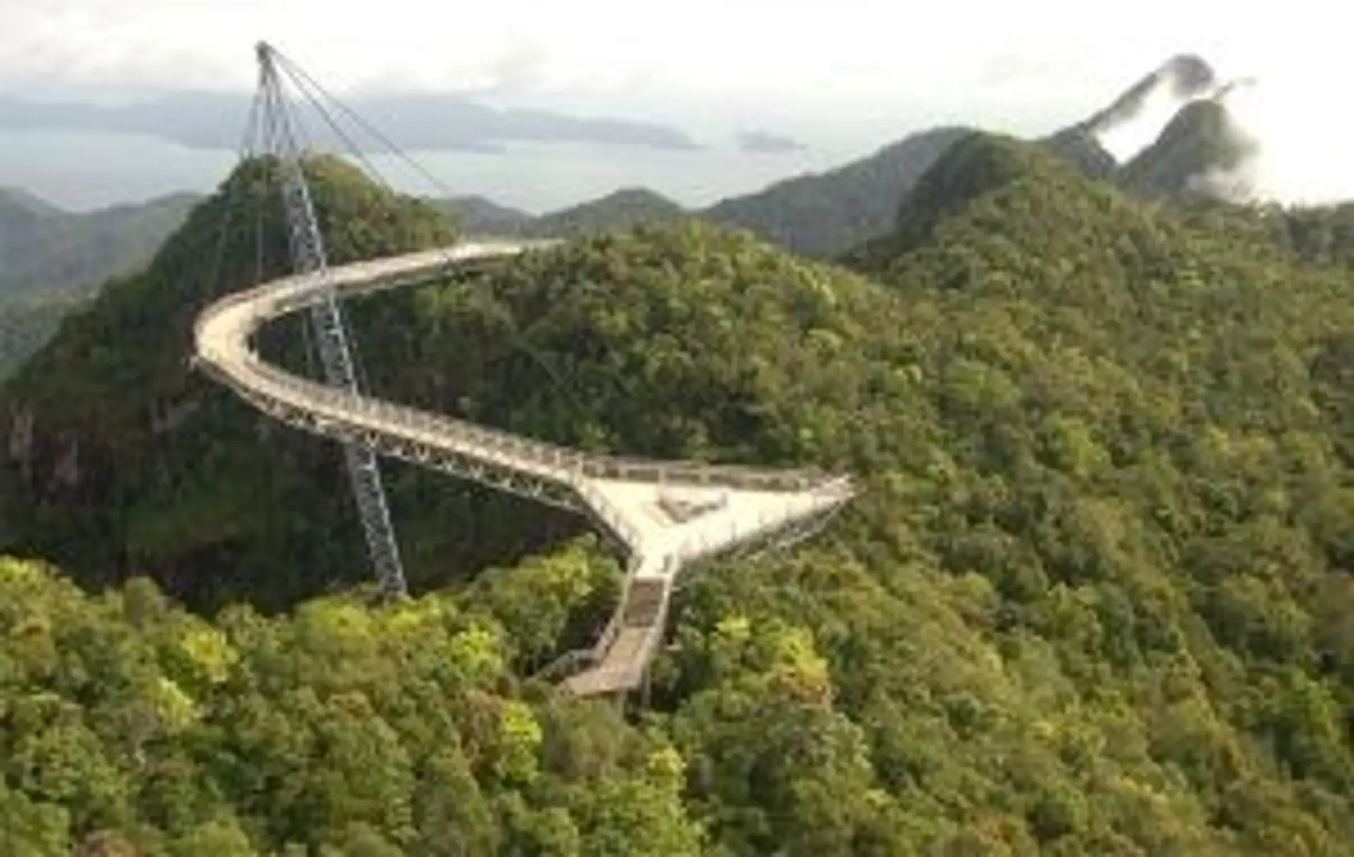 Voyage en Malaisie — Le pont suspendu incurvé Langkawi Sky Bridge surplombant la jungle luxuriante sous la brume.