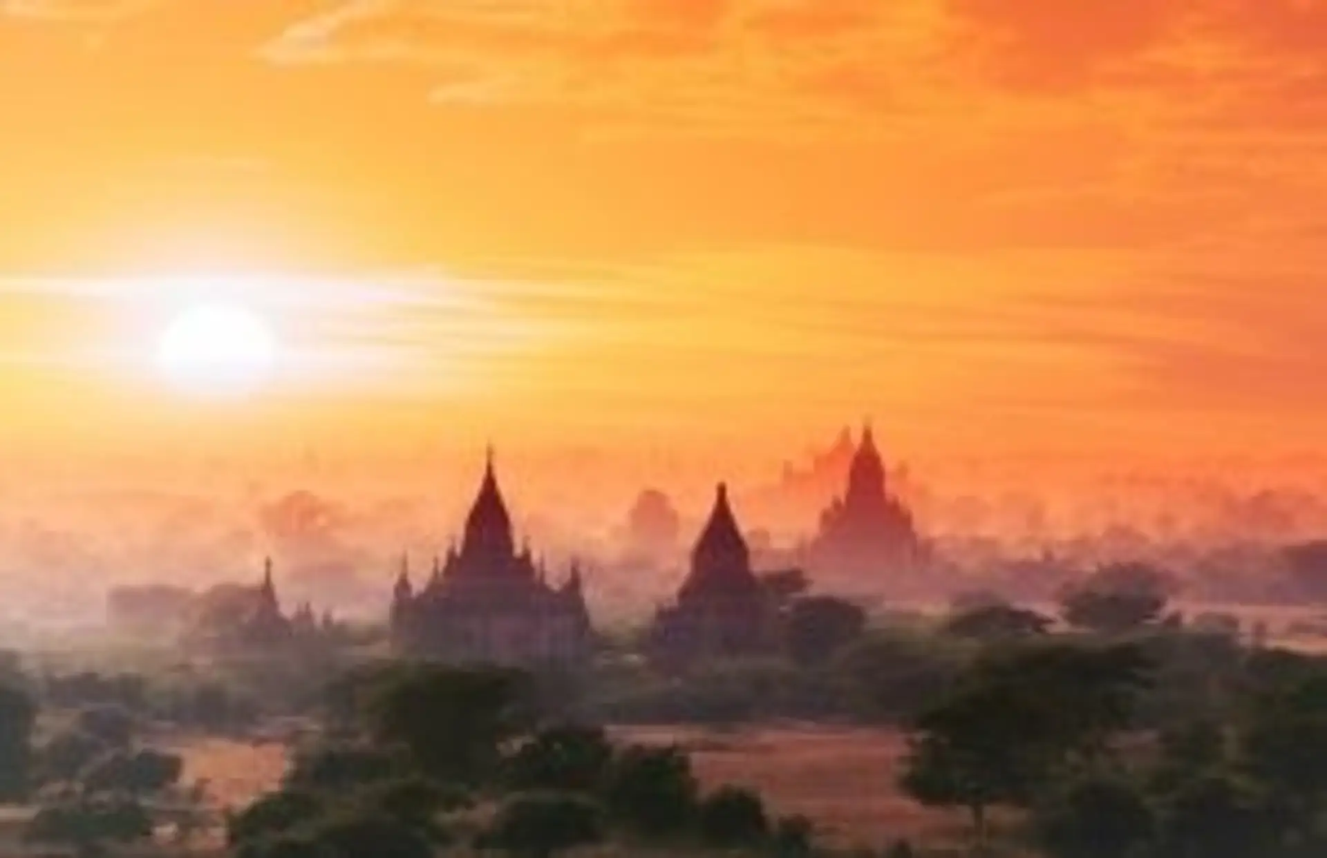 Silhouettes des temples de Bagan émergeant de la brume matinale sous un ciel orangé au lever du soleil en Birmanie.