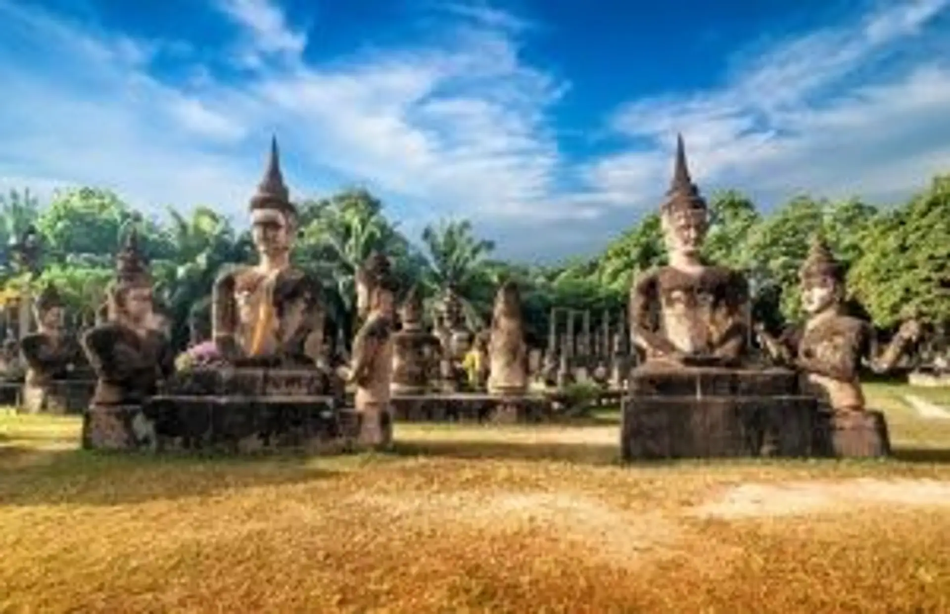 Statues de bouddhas en pierre dans un parc historique sous un ciel bleu parsemé de nuages en Thaïlande.