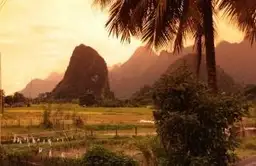 Pic calcaire au coucher du soleil surplombant une vallée verdoyante et des palmiers dans la campagne du Laos.