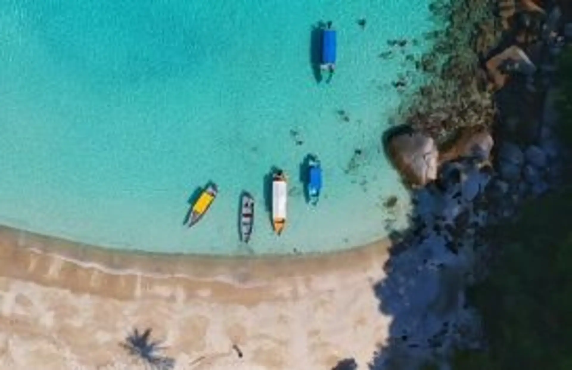 Vue aérienne d'une plage de sable blanc en Indonésie avec des bateaux traditionnels sur une eau turquoise cristalline.