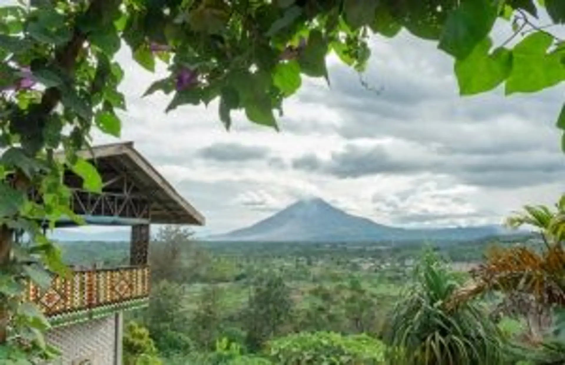 Vue panoramique sur un volcan de Sumatra depuis un balcon fleuri sous un ciel nuageux