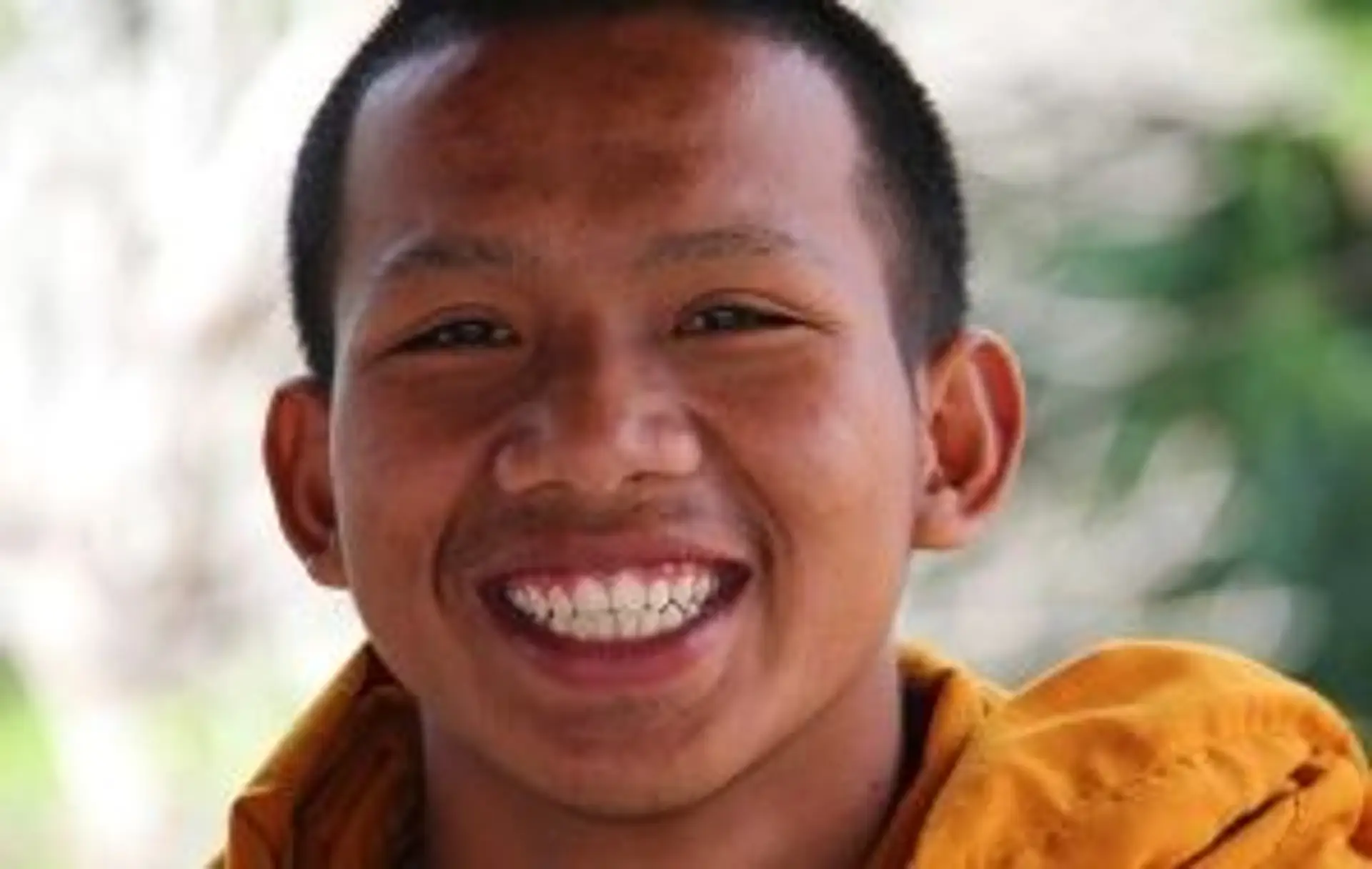 Portrait d'un jeune moine thaïlandais souriant illustrant la bienveillance et l'accueil en Thaïlande