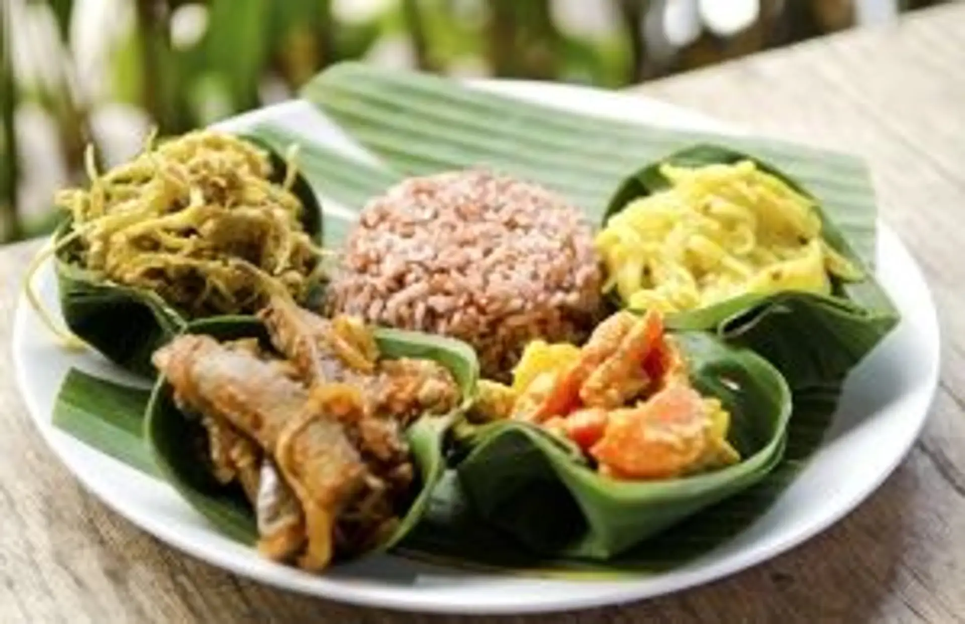 Gastronomie en Indonésie : assortiment de plats traditionnels servis sur une feuille de bananier avec riz rouge.