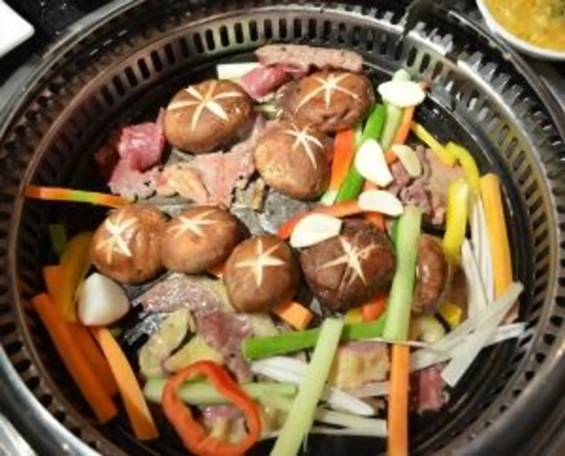 Barbecue mongol traditionnel avec viandes grillées, champignons et légumes frais sur une plaque chauffante.