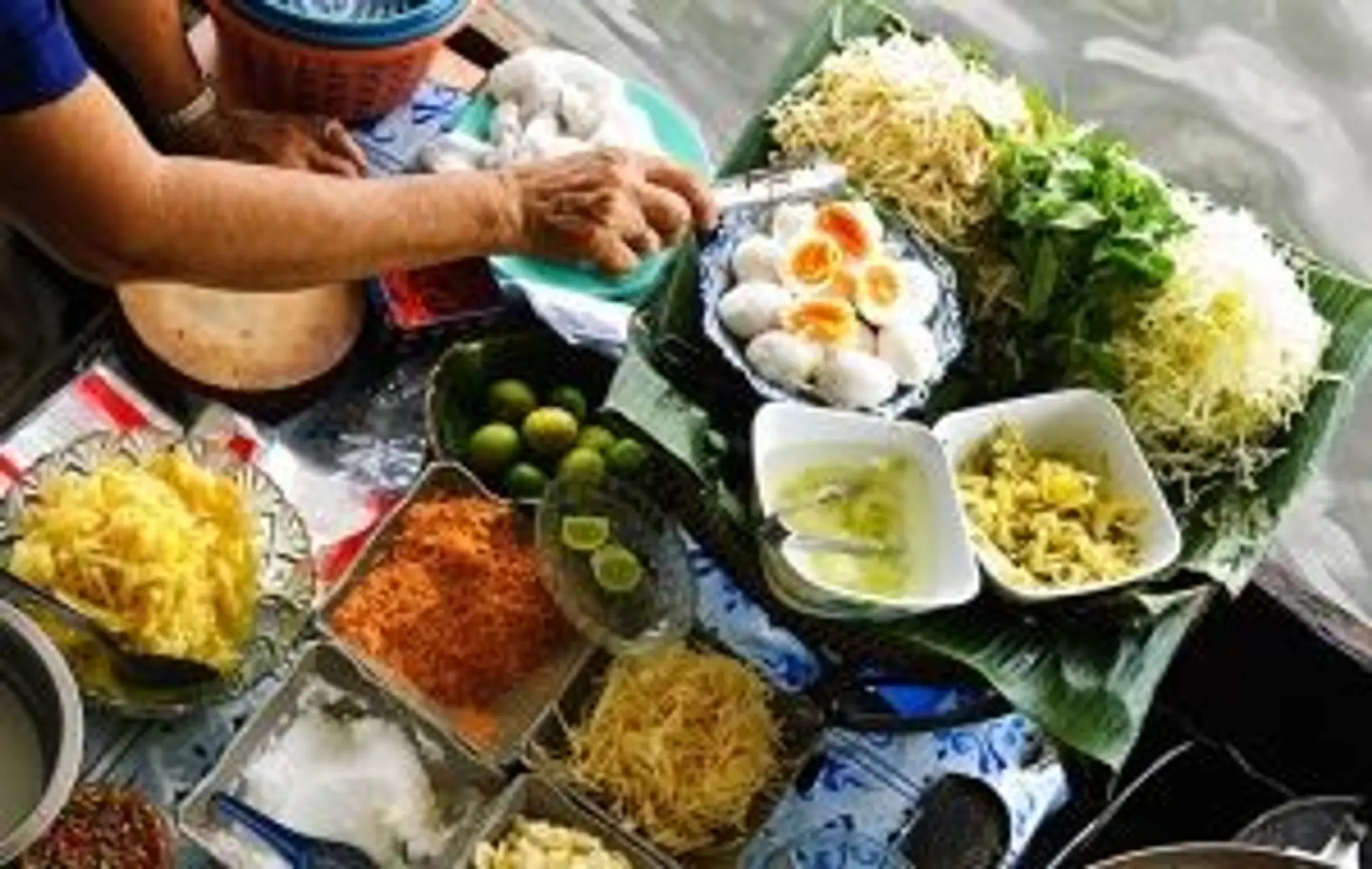 Préparation de plats thaïlandais traditionnels avec herbes fraîches, œufs, nouilles et épices sur un étal de marché local.