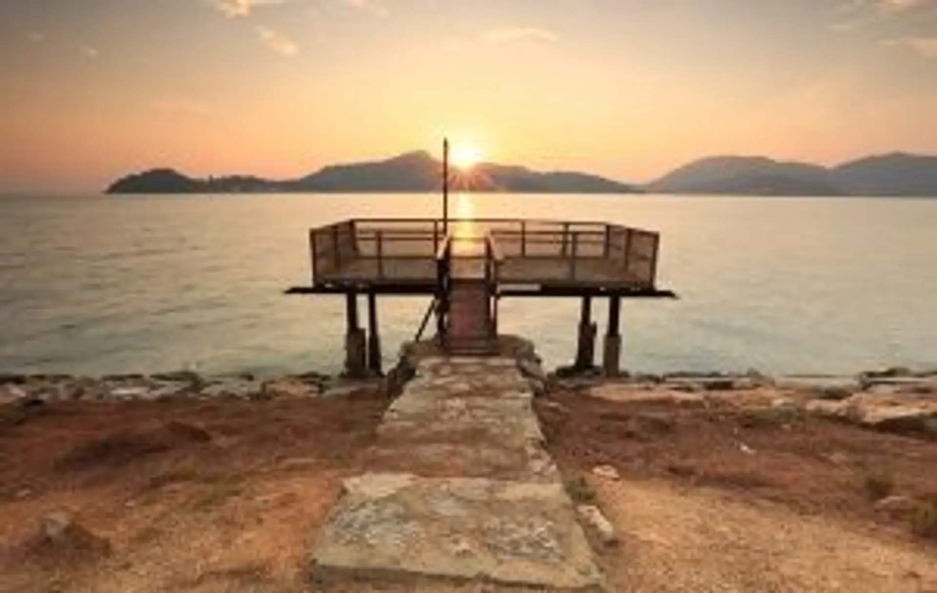 Ponton en bois s'avançant sur une mer calme au coucher du soleil face aux îles de la côte est de la Malaisie.