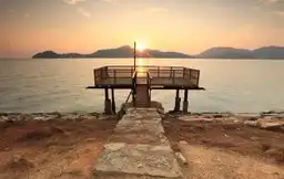 Ponton en bois s'avançant sur une mer calme au coucher du soleil face aux îles de la côte est de la Malaisie.