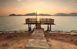 Ponton en bois s'avançant sur une mer calme au coucher du soleil face aux îles de la côte est de la Malaisie.