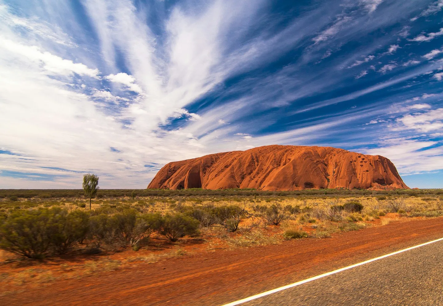 Monolithe d'Uluru se dressant dans le désert rouge sous un ciel bleu