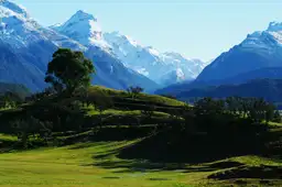Paysage verdoyant bordé par les sommets enneigés des Alpes du Sud sous un ciel bleu en Nouvelle-Zélande.