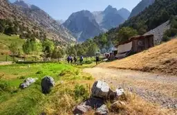 Groupe de randonneurs sur un sentier des monts Fan vers une maison traditionnelle au Tadjikistan