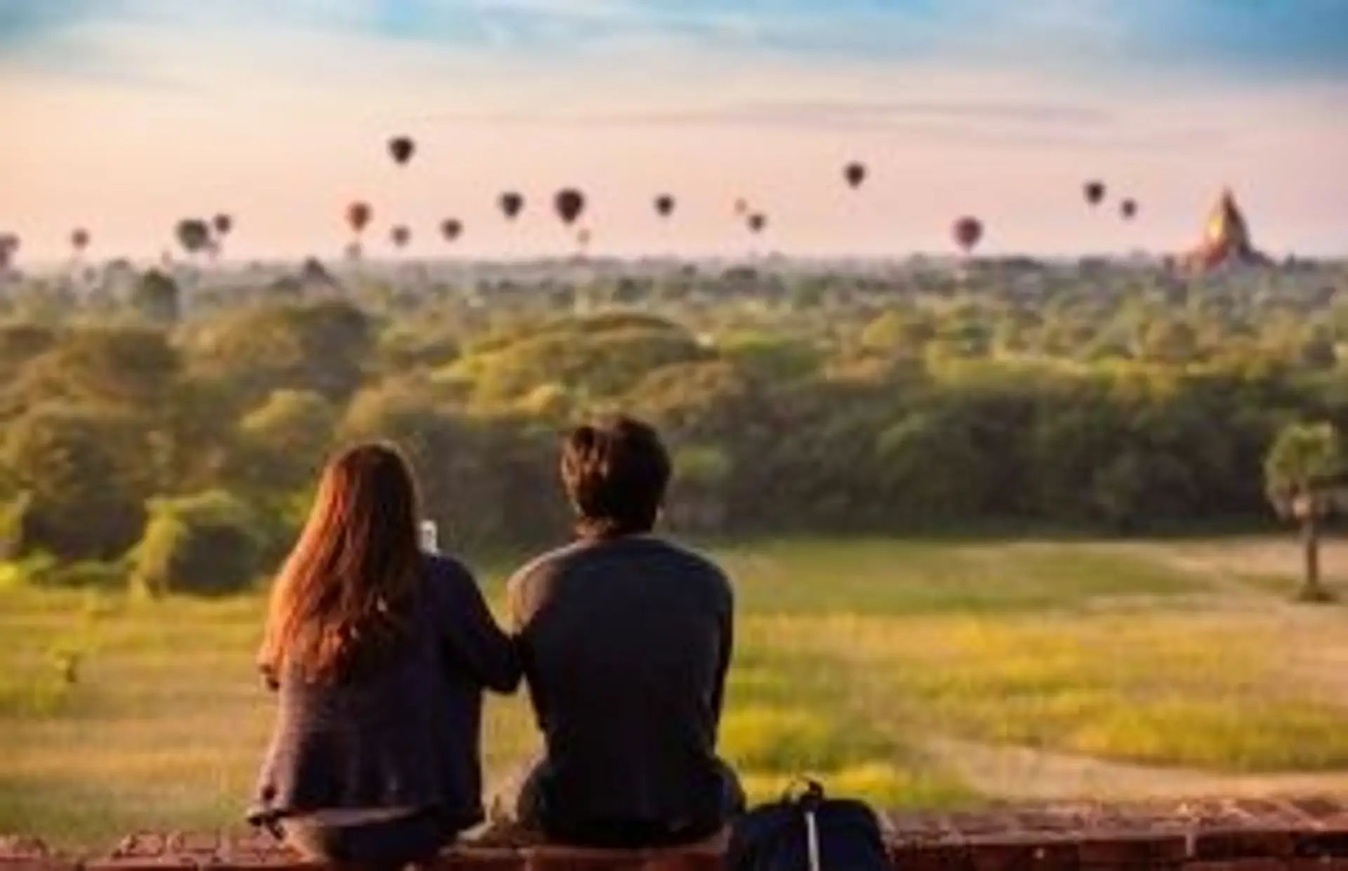 Voyage en Birmanie — Couple admirant le lever de soleil sur les temples de Bagan avec des montgolfières au loin.