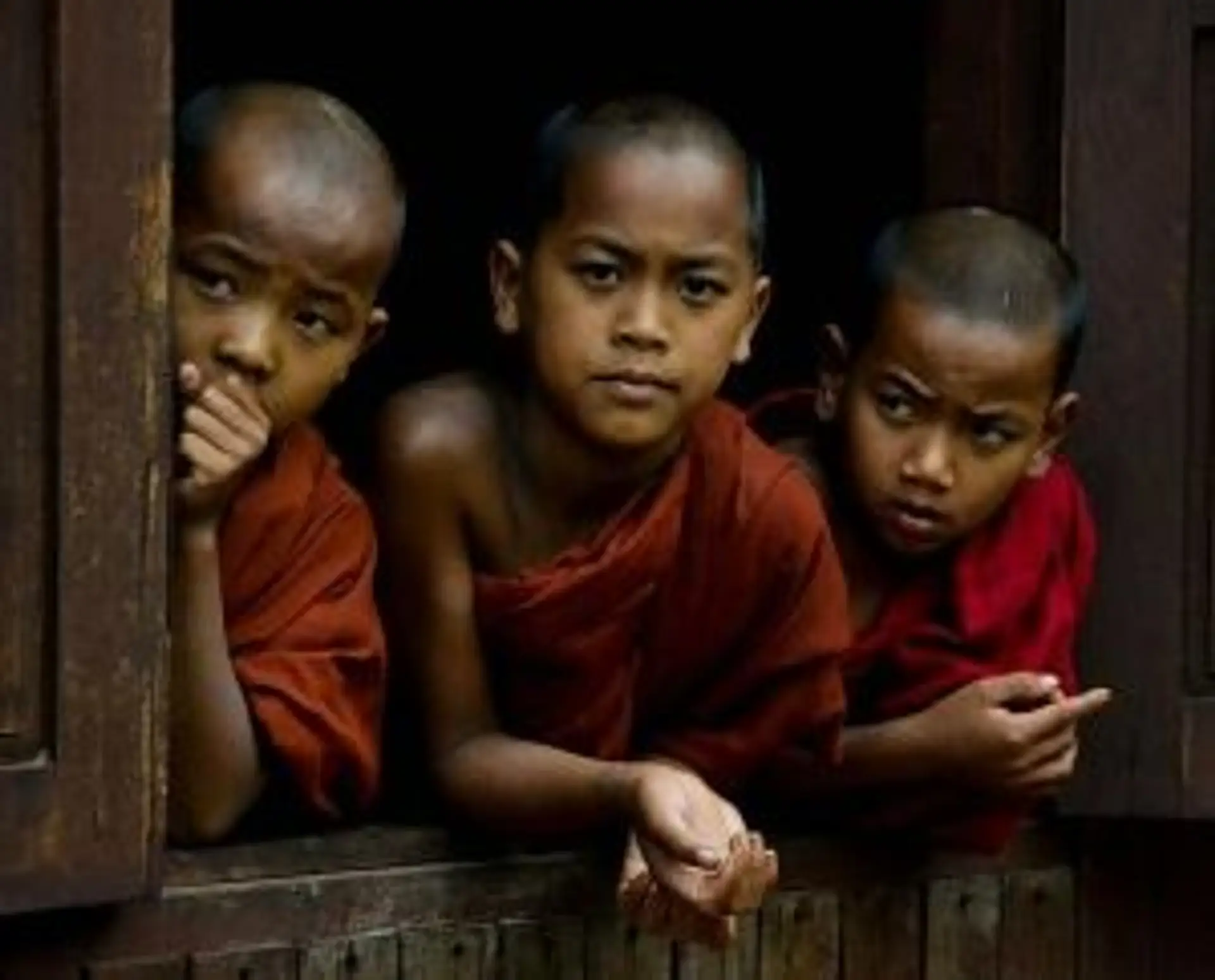 Travel in Asia - Three young, bald novice monks in a temple window.