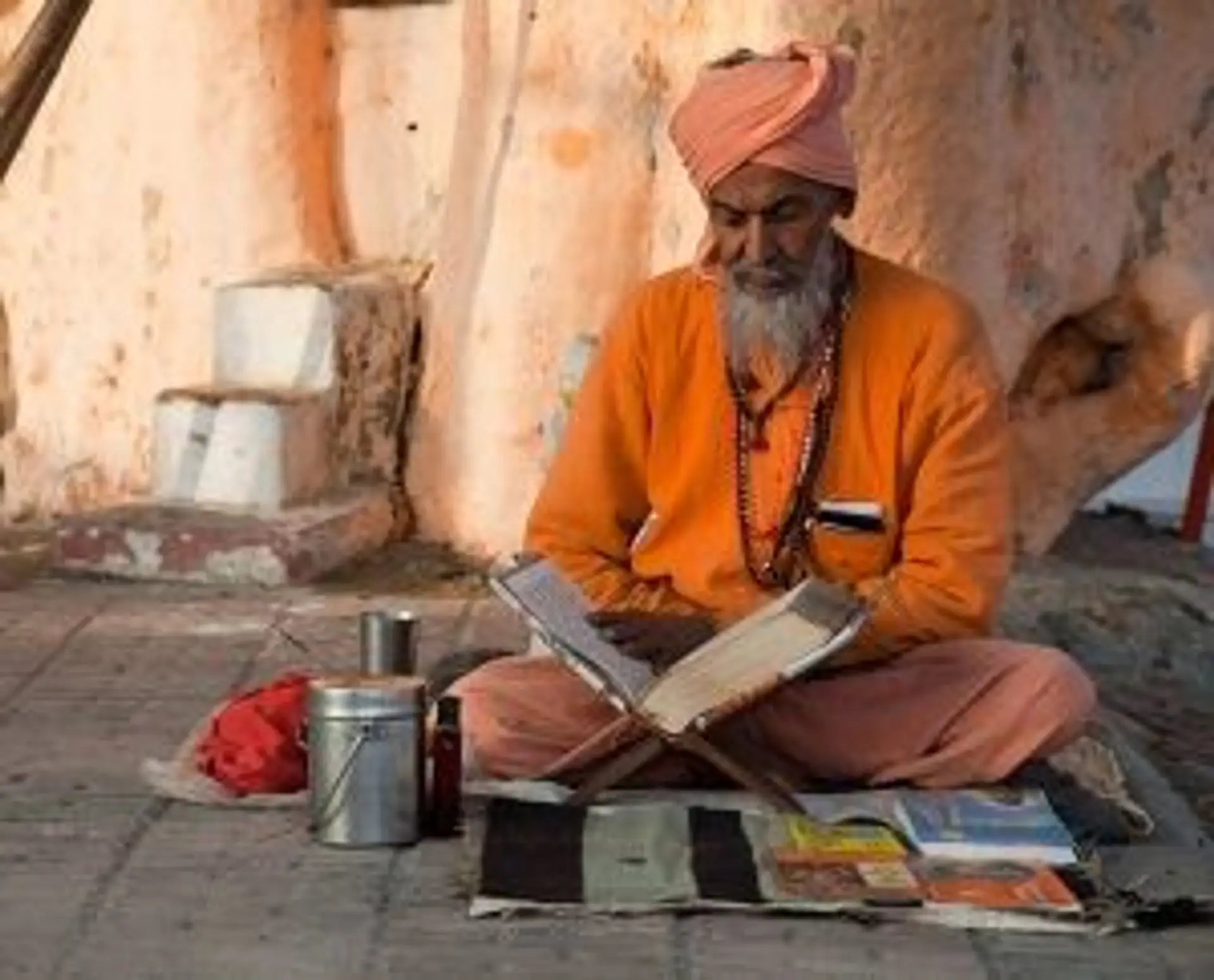 Travel in Asia - A Hindu holy man reading from texts while seated and wearing orange clothing