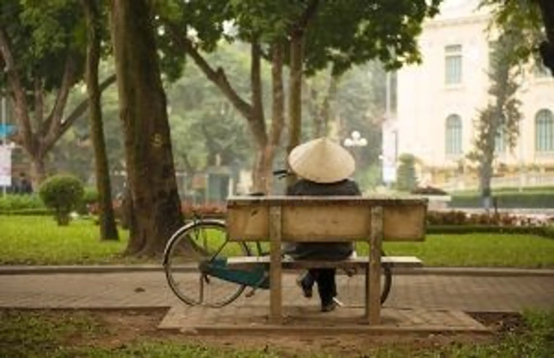 Travel in Asia - Person sitting on a bench with a bicycle nearby in a city park in Hanoi, Vietnam