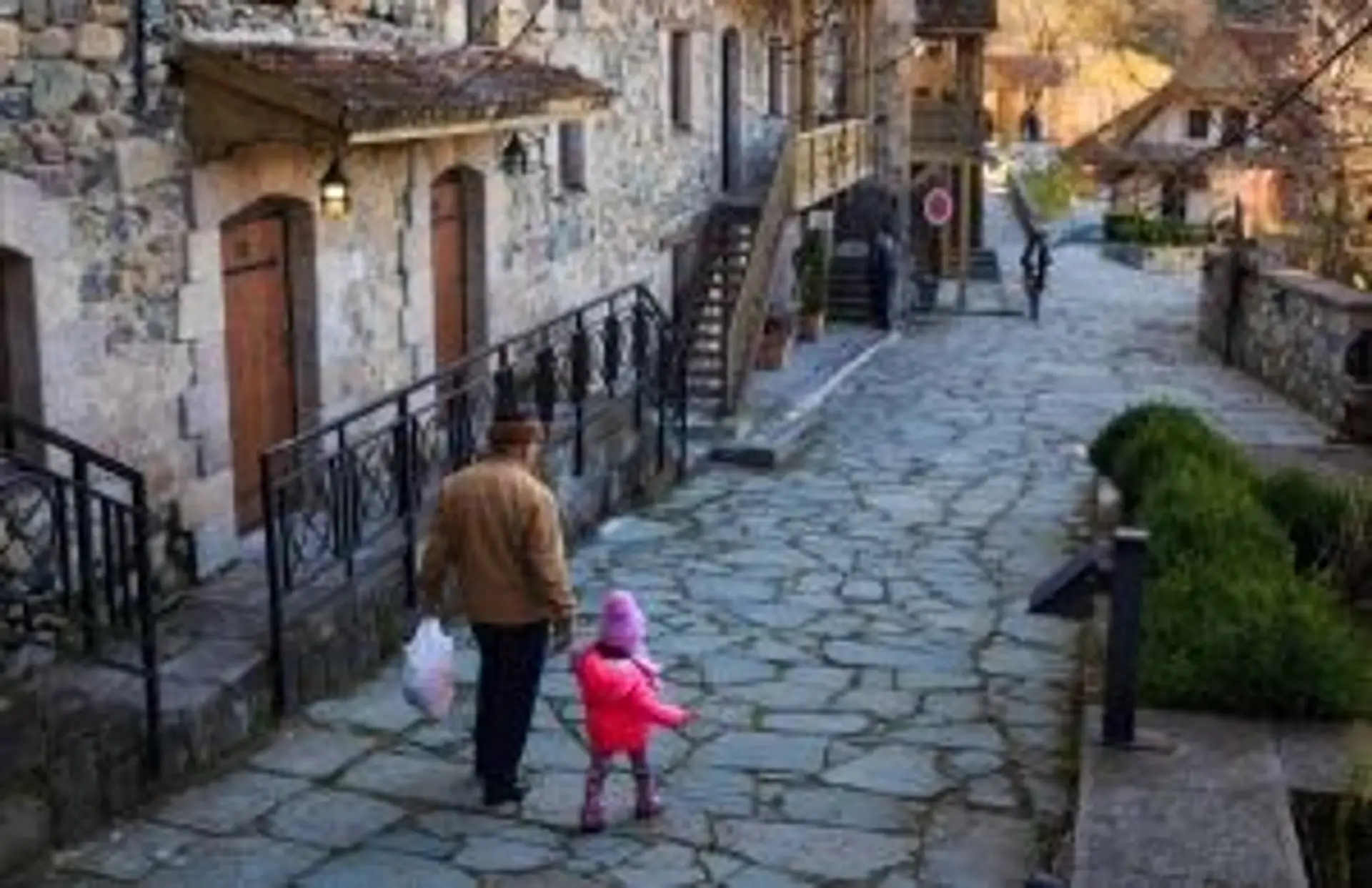 Un homme et un enfant marchant dans une ruelle pavée d'un village traditionnel en Arménie