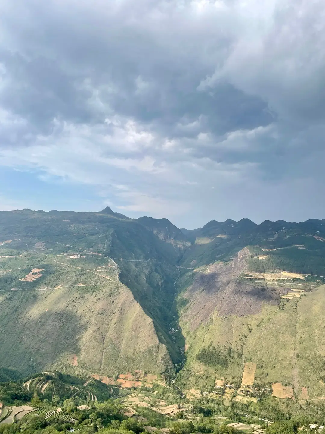 Un panorama impressionnant sur un canyon profond et des montagnes rocheuses escarpées sous un ciel nuageux au Vietnam.