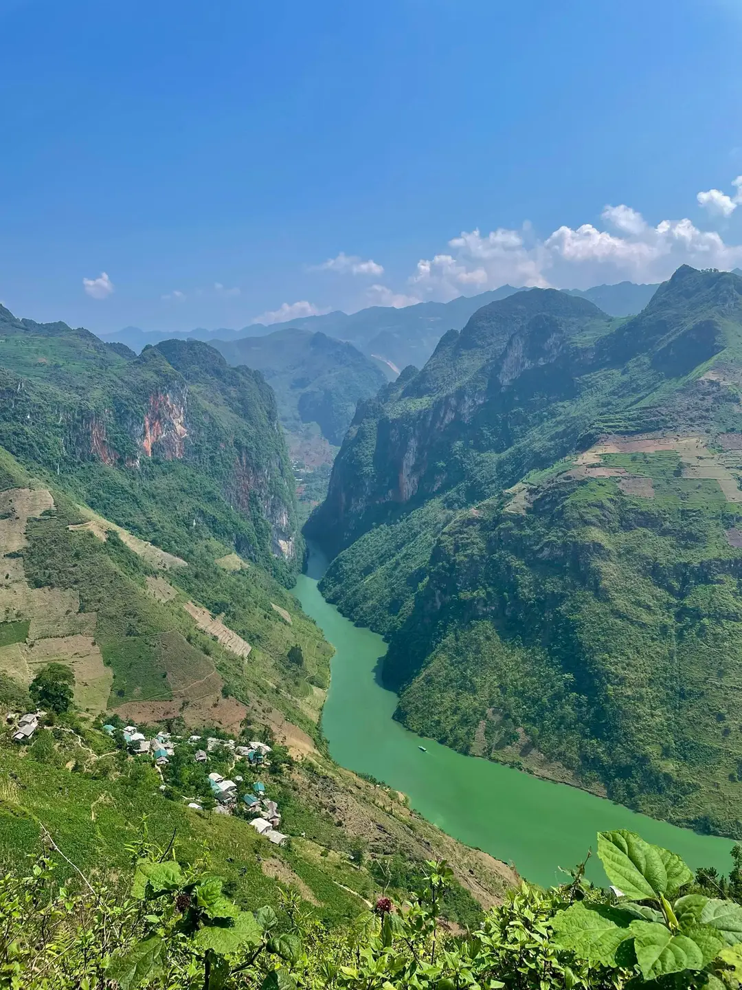 Une rivière aux eaux vert émeraude coule au fond d'un gigantesque canyon escarpé entouré de hautes montagnes verdoyantes sous un ciel bleu parsemé de nuages au Vietnam.